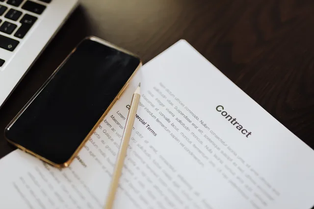 Close-up of a contract document alongside a smartphone and laptop, ideal for business concepts. Anforderungsprofil für SaaS erstellen: Funktionen, Schnittstellen und Daten